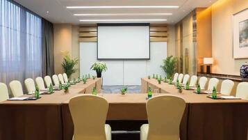 A conference room with a long table, chairs, a projector screen, and potted plants.