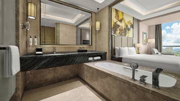 Un baño de hotel moderno con un lavamanos grande de mármol, una bañera y un espejo amplio.
