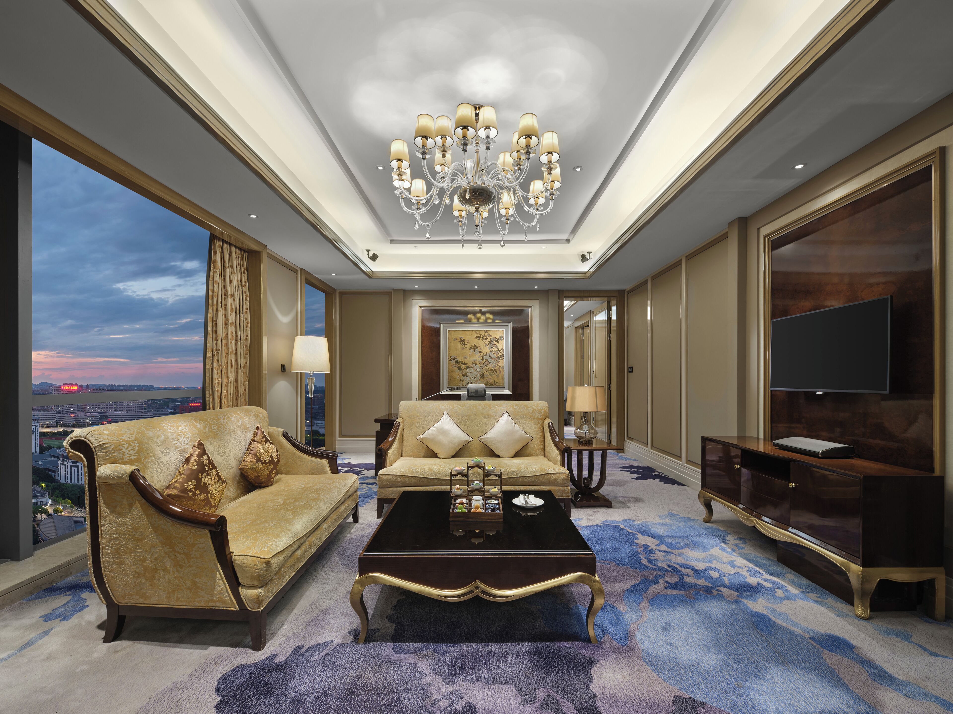 A spacious living room with a large chandelier, a sofa, a coffee table, and a TV.
