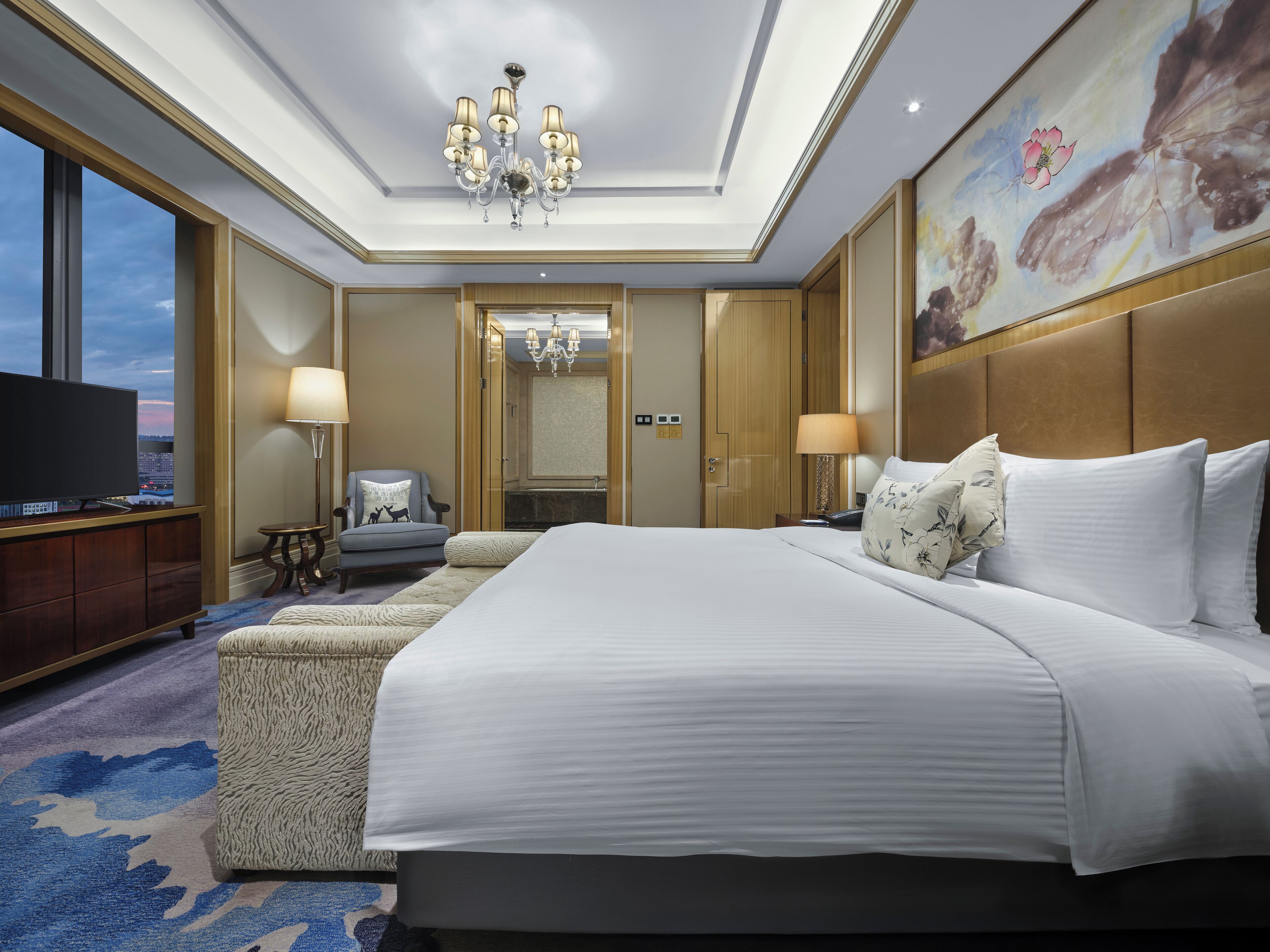 Une chambre d’hôtel avec un grand lit, une télévision, une chaise, un bureau et un tableau au mur.