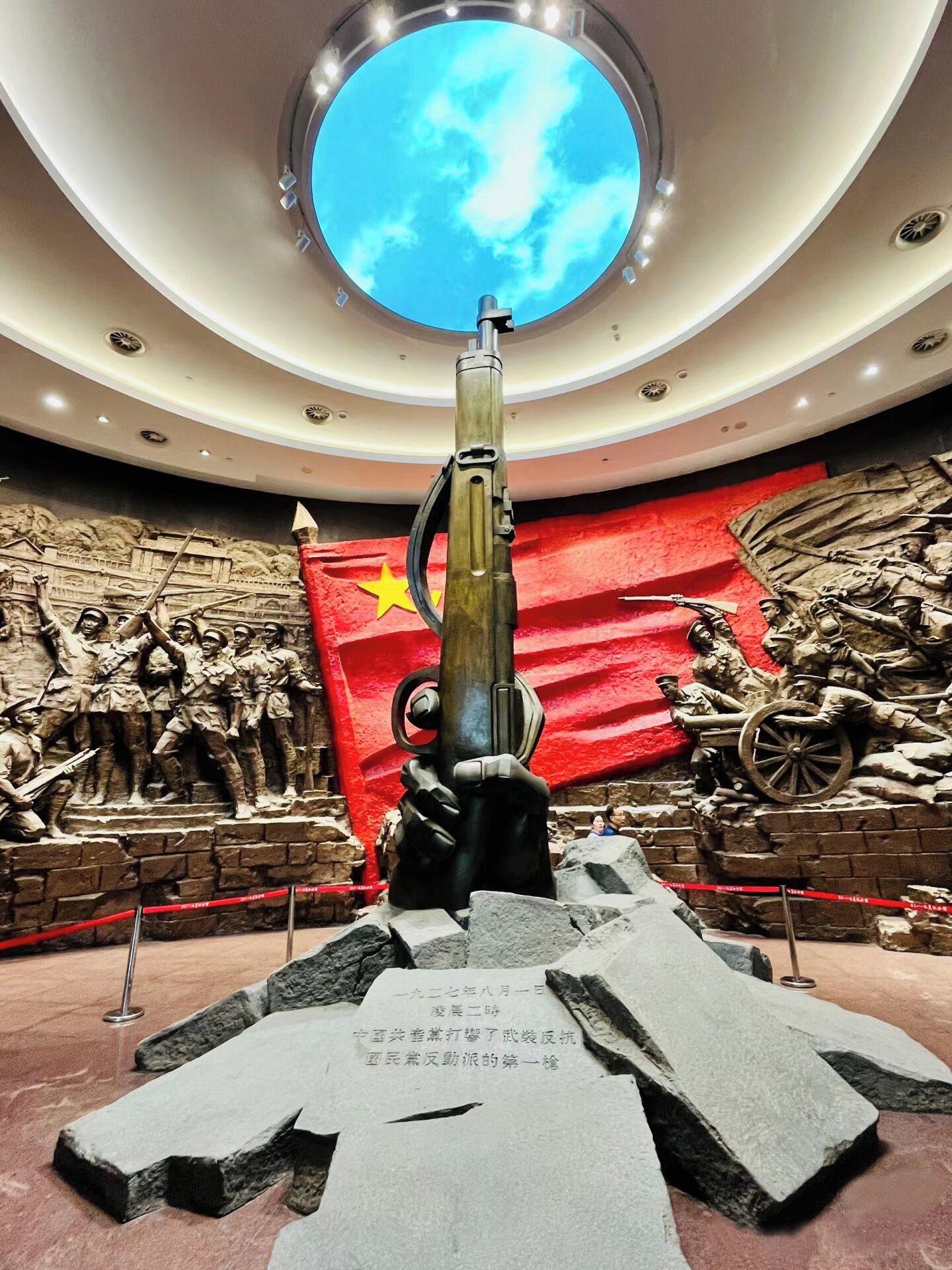 Uma exposição de museu com uma grande escultura de uma arma, uma bandeira vermelha e um relevo retratando soldados.