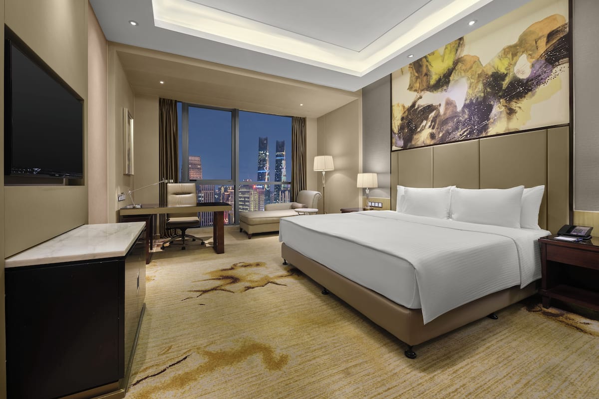 Ein modernes Hotelzimmer mit einem großen Bett, einem Schreibtisch, einem Stuhl und Blick auf die Stadt.