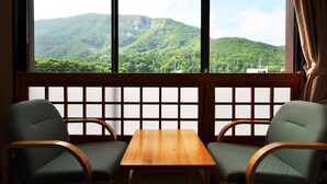 A room with two chairs and a table, a wooden partition with a grid pattern, and a view of green mountains through large windows. - Hotel Ryusendo Aizan (Iwaizumi)