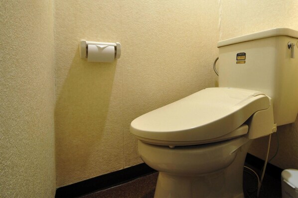 Un inodoro con asiento y tapa blancos, un dispensador de papel higiénico en la pared y una etiqueta de la marca TOTO en el tanque.