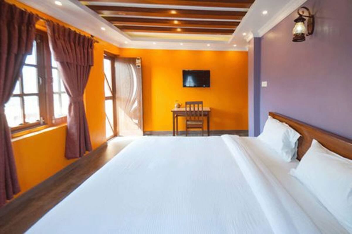 A hotel room with a large bed, a television on the wall, and a window with curtains.