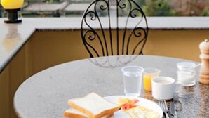 A dining table with a plate of food, a glass of water, and a cup, set against a view of trees and buildings. - Be Here Now Guest House (Kathmandu)