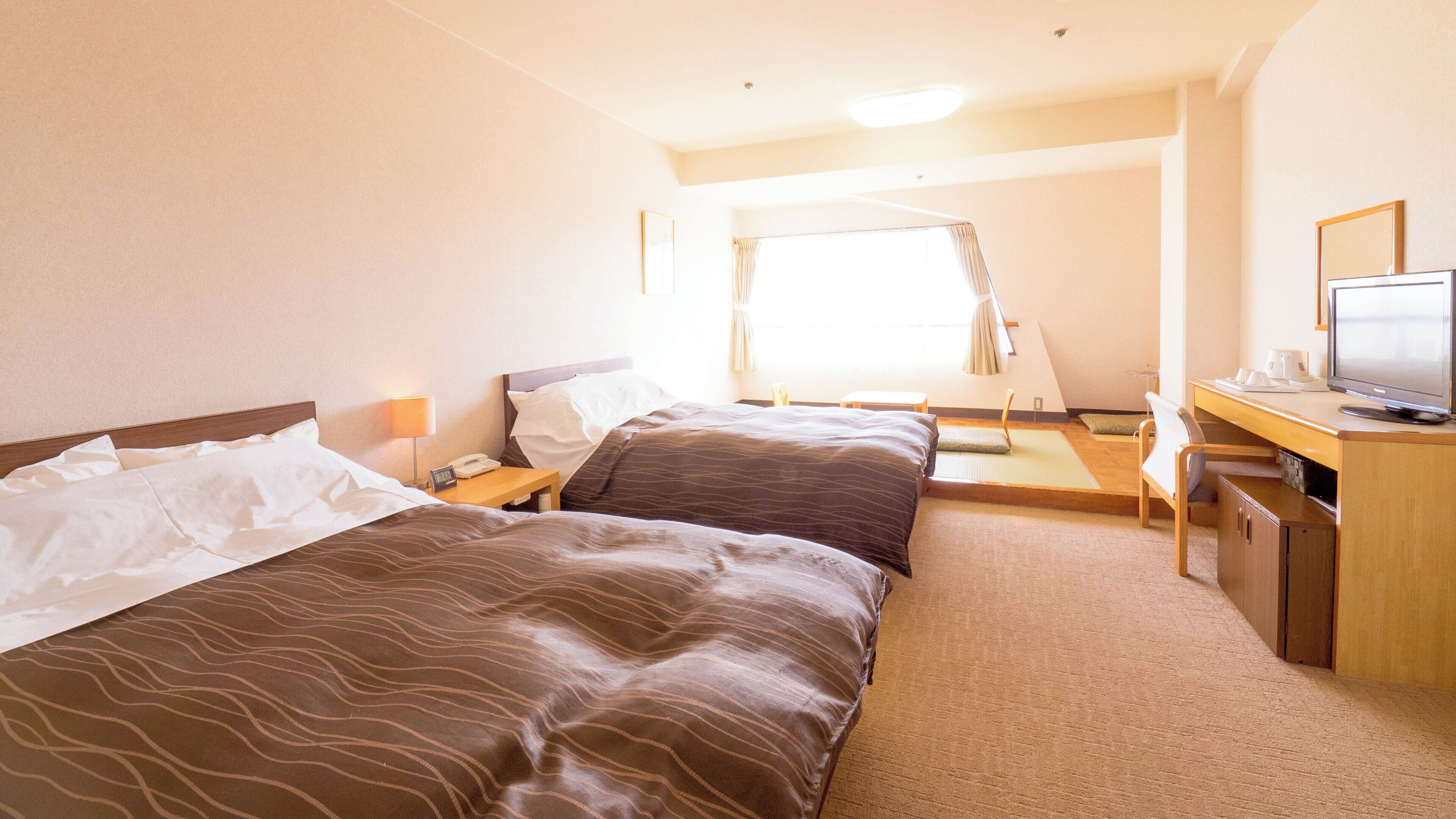 A hotel room with two beds, a desk with a television, and a window with curtains.