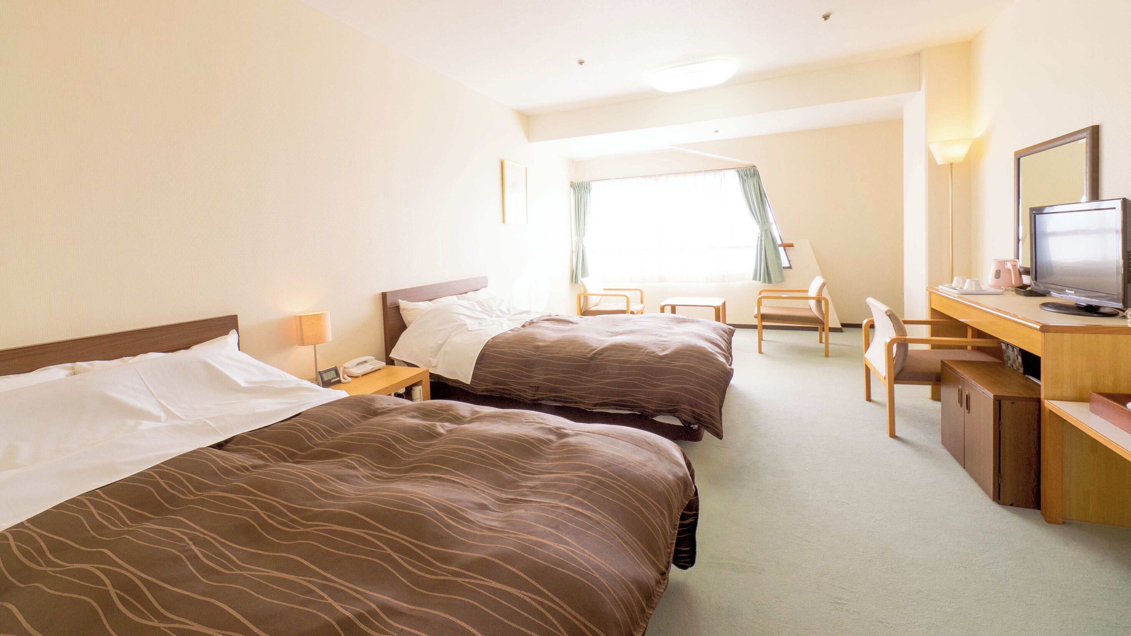 A hotel room with two beds, a desk with a computer, a chair, and a window with curtains.