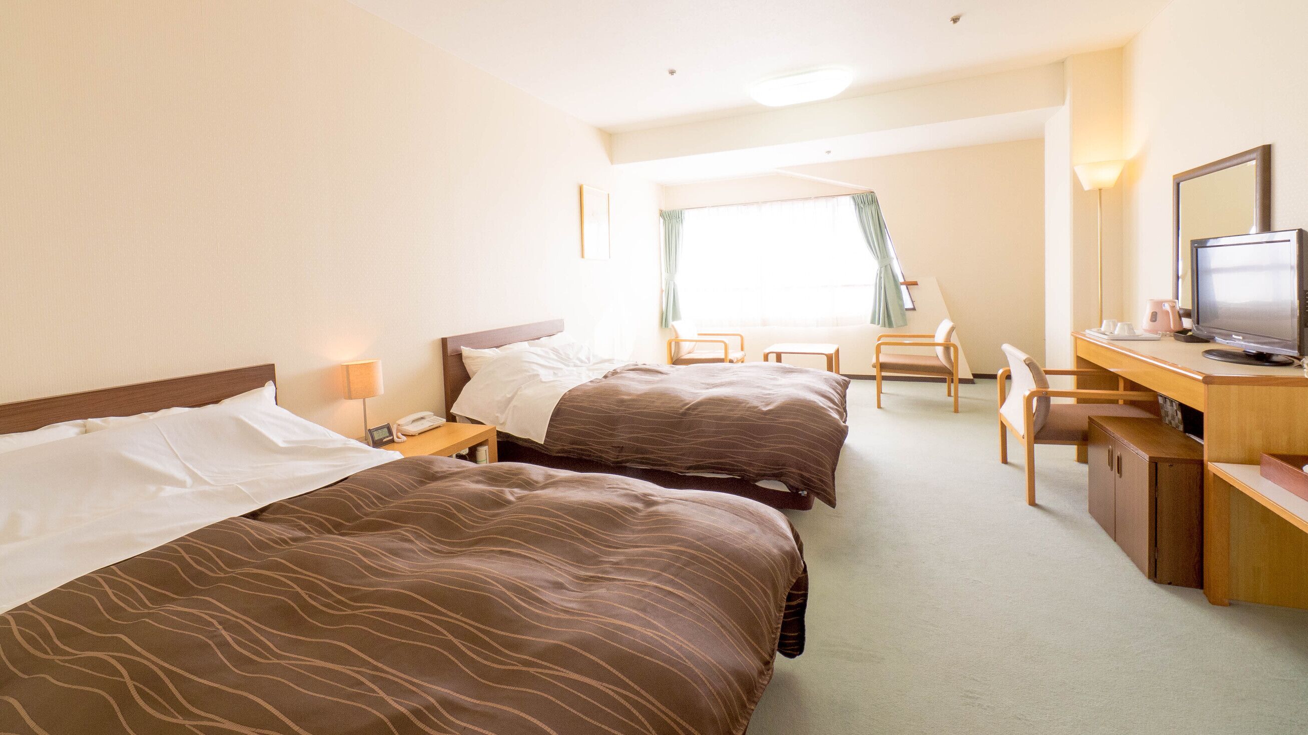 A hotel room with two beds, a desk with a computer, a chair, and a window with curtains.