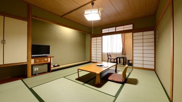 Une pièce de style japonais traditionnel, avec un sol recouvert de tatamis, un téléviseur, une petite table basse et des portes coulissantes.