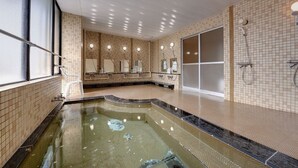 Une grande piscine intérieure avec un sol carrelé, une paroi en verre et un espace douche.