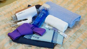 A bed with a patterned bedspread, a blue towel, a purple pillow, a blue bottle, a white box, and a purple item. - Miyako Hotel Sawadaya (Miyako)