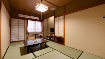 A traditional Japanese room with tatami flooring, a low table, a television, and sliding doors.