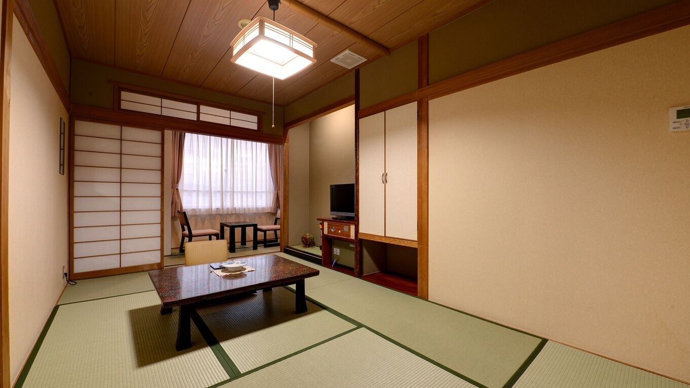 Una habitación japonesa tradicional con suelo de tatami, una mesa baja, puertas correderas y un televisor.