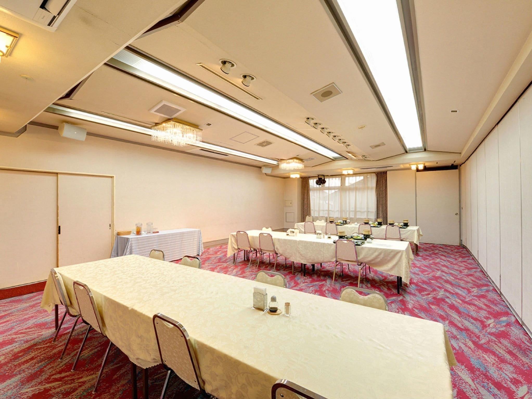 A conference room with multiple tables and chairs, a carpeted floor, and a chandelier.