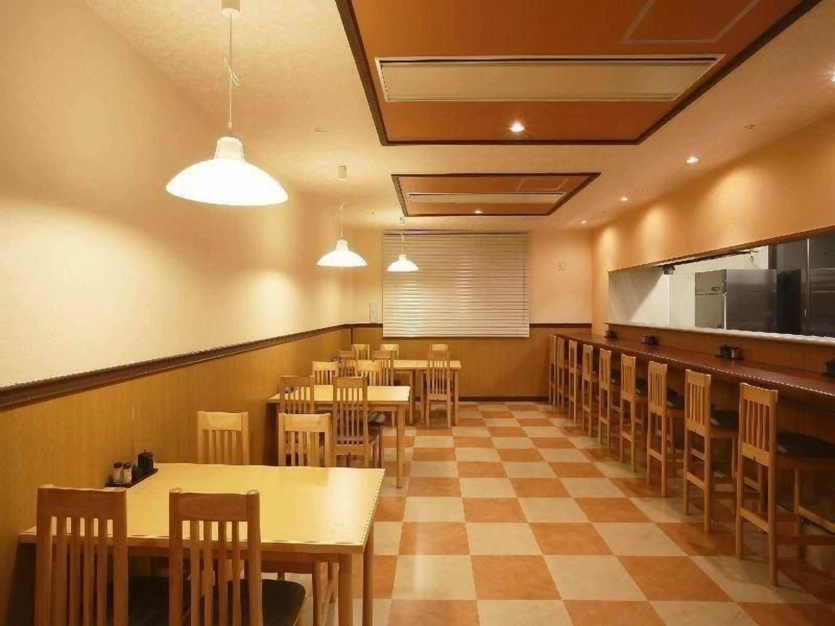 A dining area with wooden tables and chairs, a checkered floor, pendant lighting, and a kitchen counter.