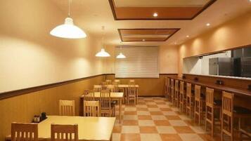 A dining area with wooden tables and chairs, a checkered floor, pendant lighting, and a kitchen counter.