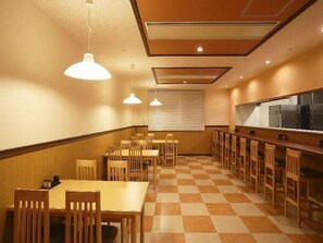 Uma sala de jantar com mesas e cadeiras de madeira, chão xadrez, iluminação pendente e balcão de cozinha.