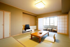 Una habitación japonesa tradicional con suelo de tatami, una mesa baja con un cuenco, un televisor y puertas correderas.