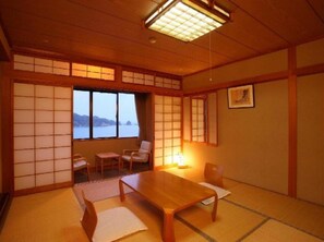 Um quarto japonês tradicional com tatames, uma mesa baixa e vista para o mar.