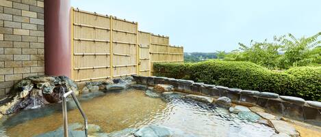 A traditional Japanese onsen with a stone bath, bamboo fence, and a view of the surrounding greenery.