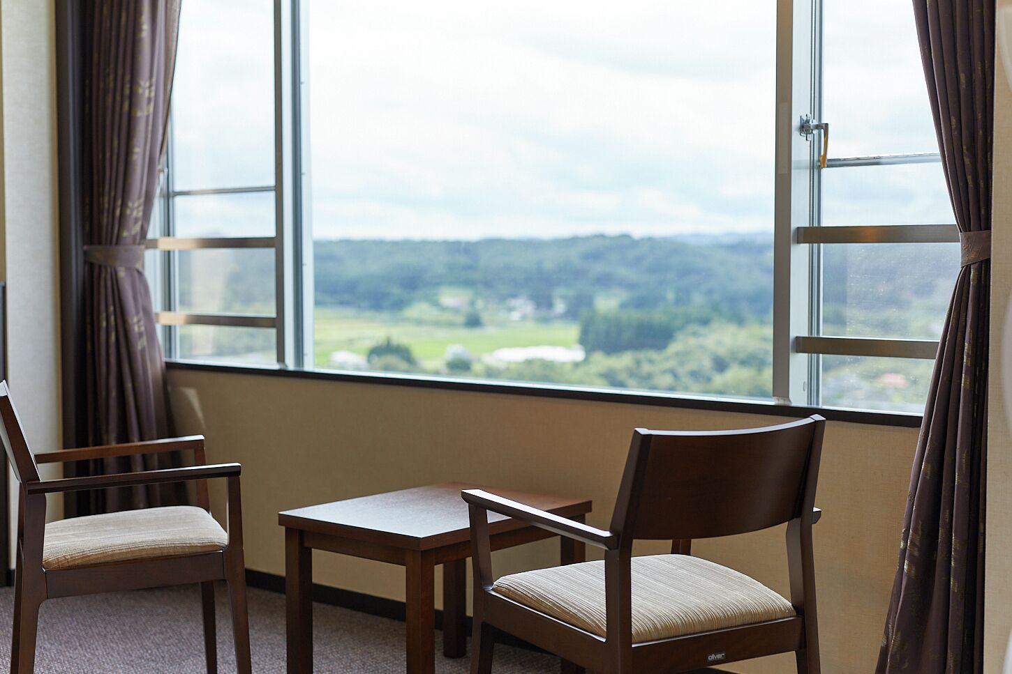 A room with a large window, two chairs, and a small table.