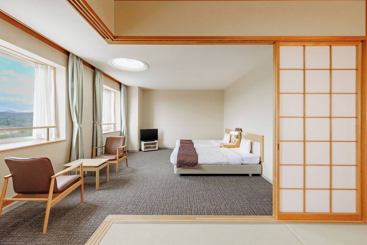 Habitación de hotel con cama, escritorio, silla, televisor y vistas al exterior.