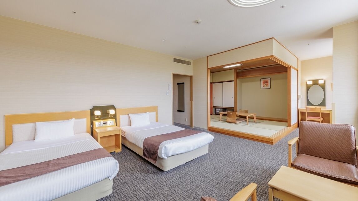 Ein Hotelzimmer mit zwei Betten, einer Sitzecke mit Stuhl und Tisch, einem Spiegel und einem kleinen Tisch mit Lampe.