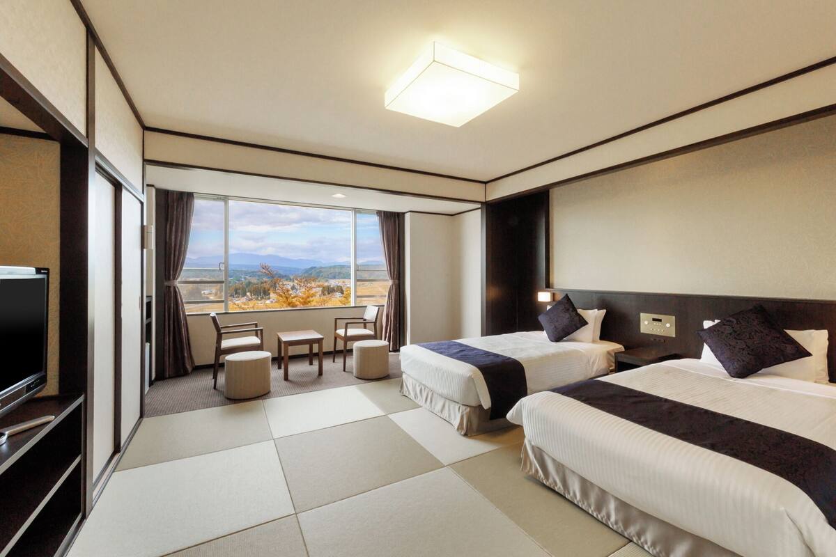 Habitación de hotel con dos camas, televisión, escritorio y vistas a la montaña.