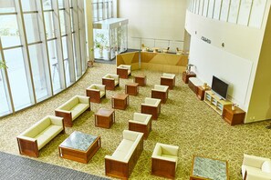 Un hall d’entrée spacieux, doté de plusieurs coins salon, d’un téléviseur et d’une cloison en verre agrémentée de plantes.