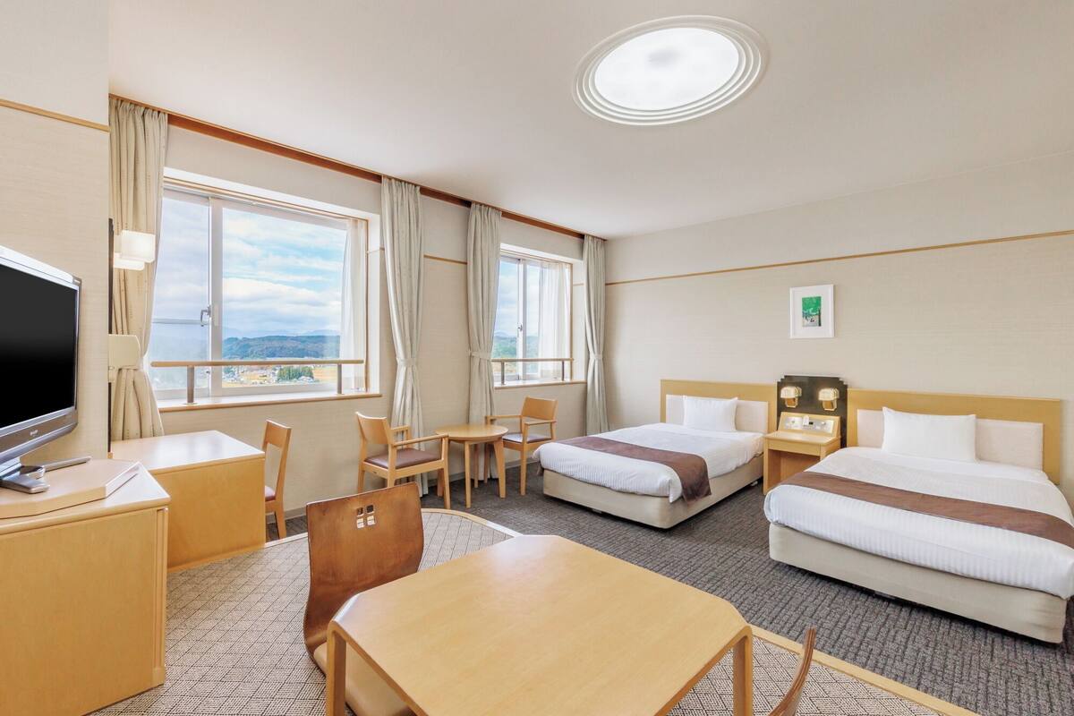 Habitación de hotel con dos camas, un escritorio con televisor, una silla y vistas a las montañas.