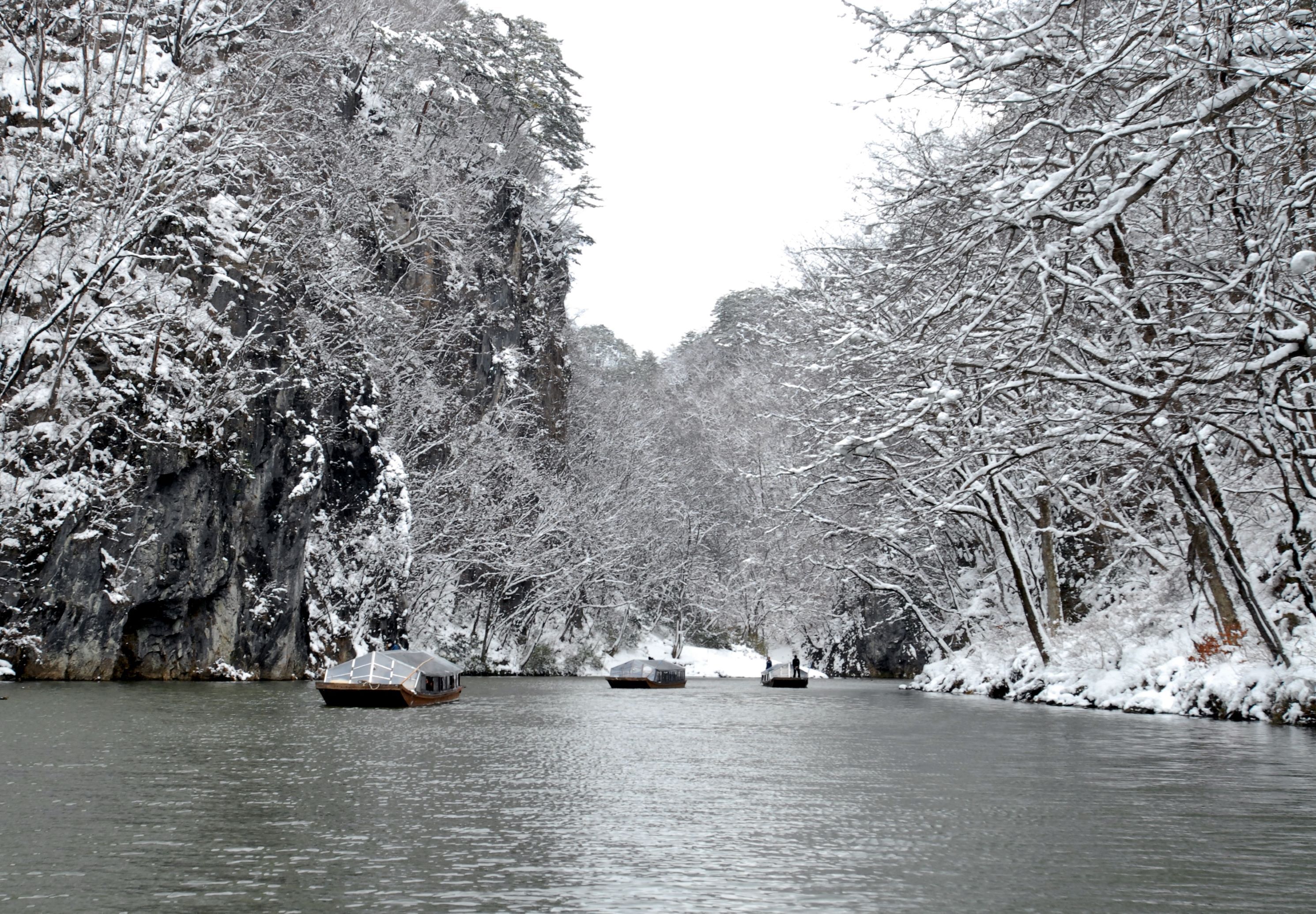 A snow-covered river with boats and dense trees on both sides.