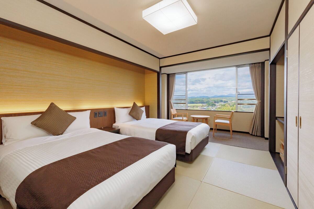 Una habitación de hotel con dos camas, una mesita y vistas al paisaje.