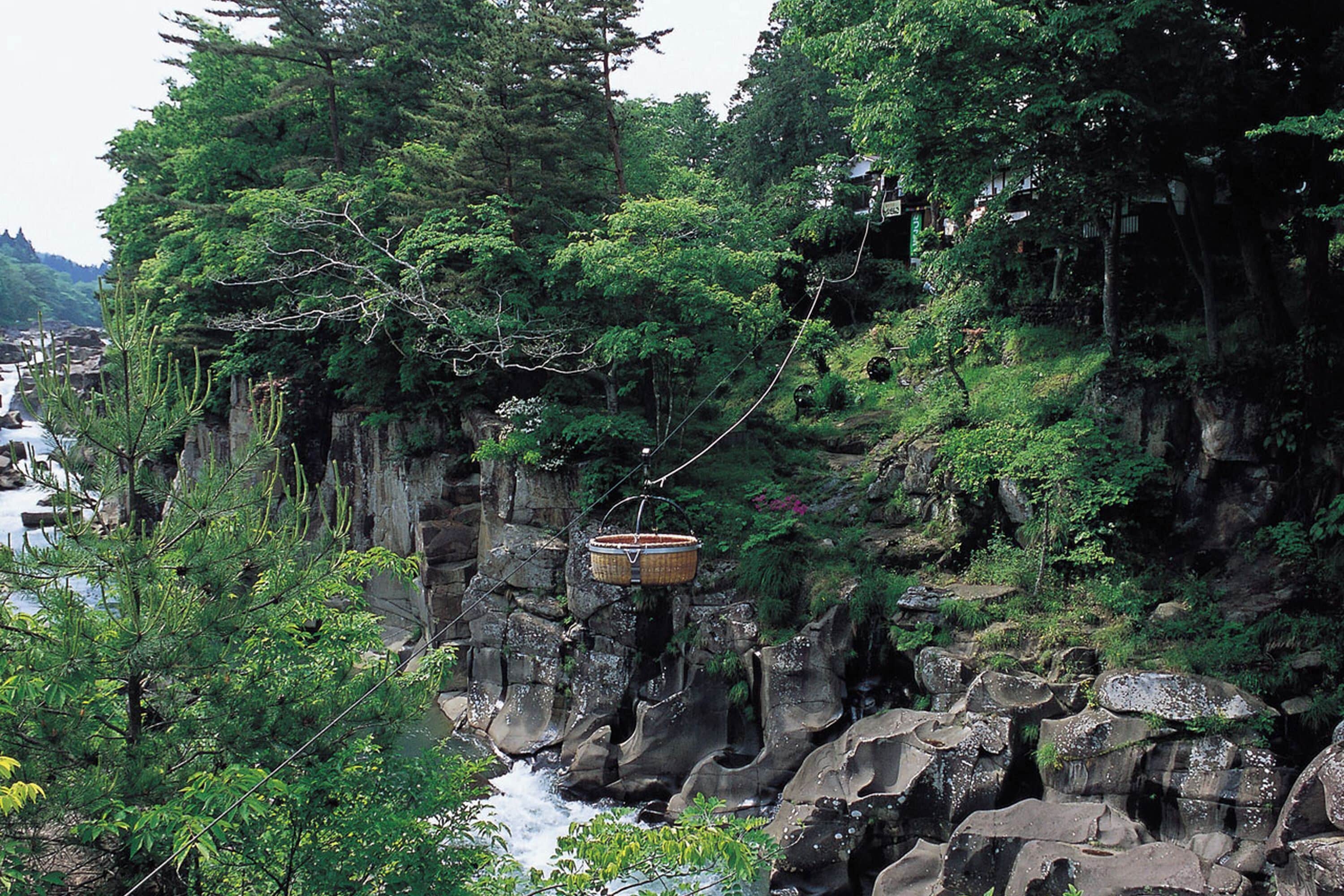 Un panier suspendu au-dessus d’une falaise rocheuse, avec une rivière en contrebas.