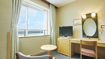 Quarto de hotel com escrivaninha, televisão, cadeira, mesa pequena e janela com cortinas.