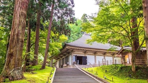 Un edificio japonés tradicional con techo inclinado, rodeado de abundante follaje y árboles altos.