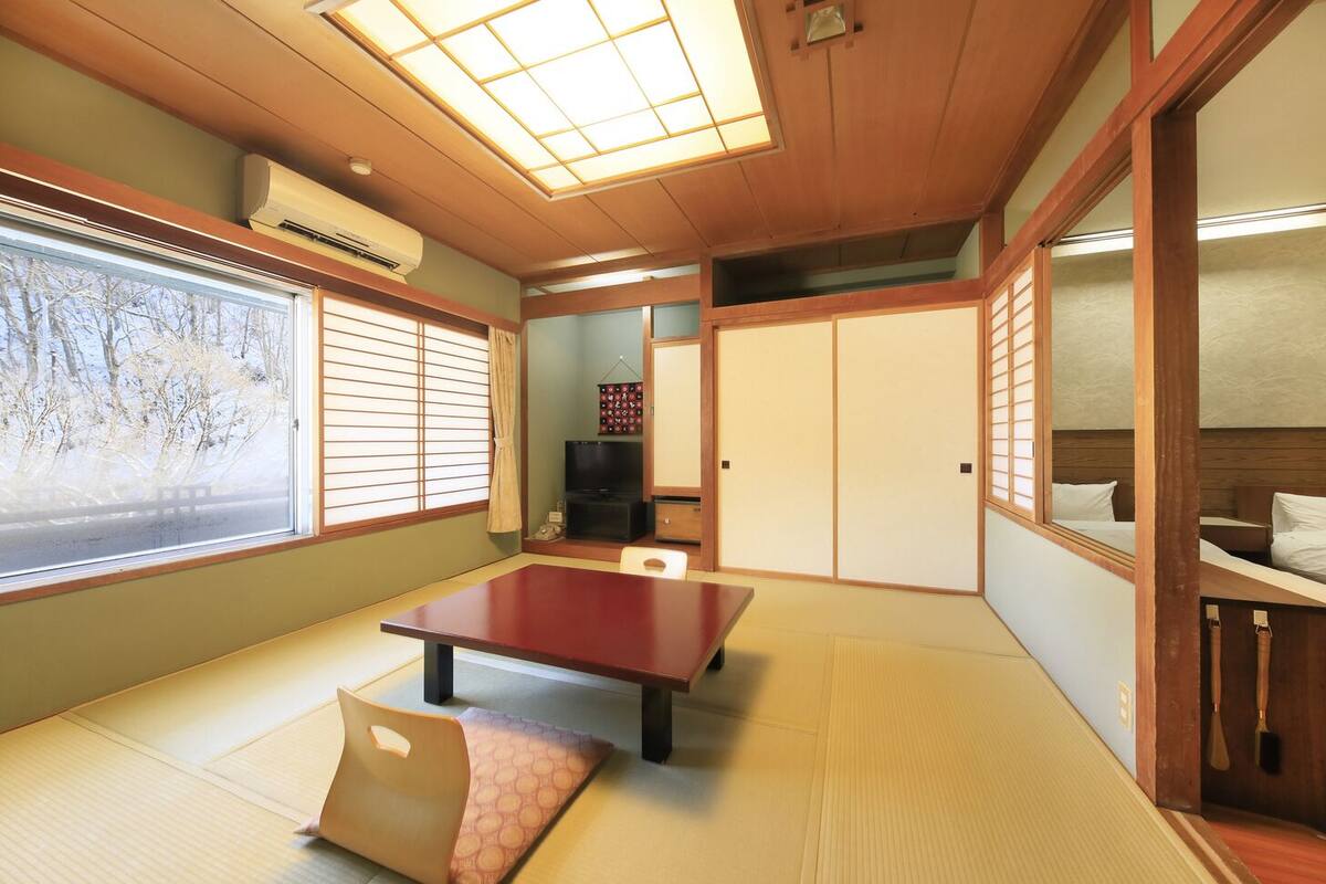 Ein traditioneller japanischer Raum mit Tatami-Bodenbelag, einem niedrigen Tisch, Schiebetüren und einem Fernseher.