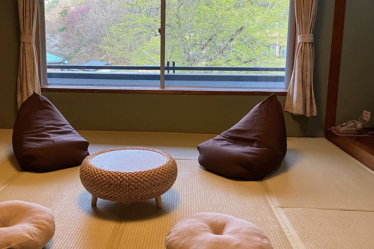 Ein Raum mit Tatami-Matten, einem runden Gewebetisch, zwei braunen Kissen und einem Telefon auf einem Beistelltisch.