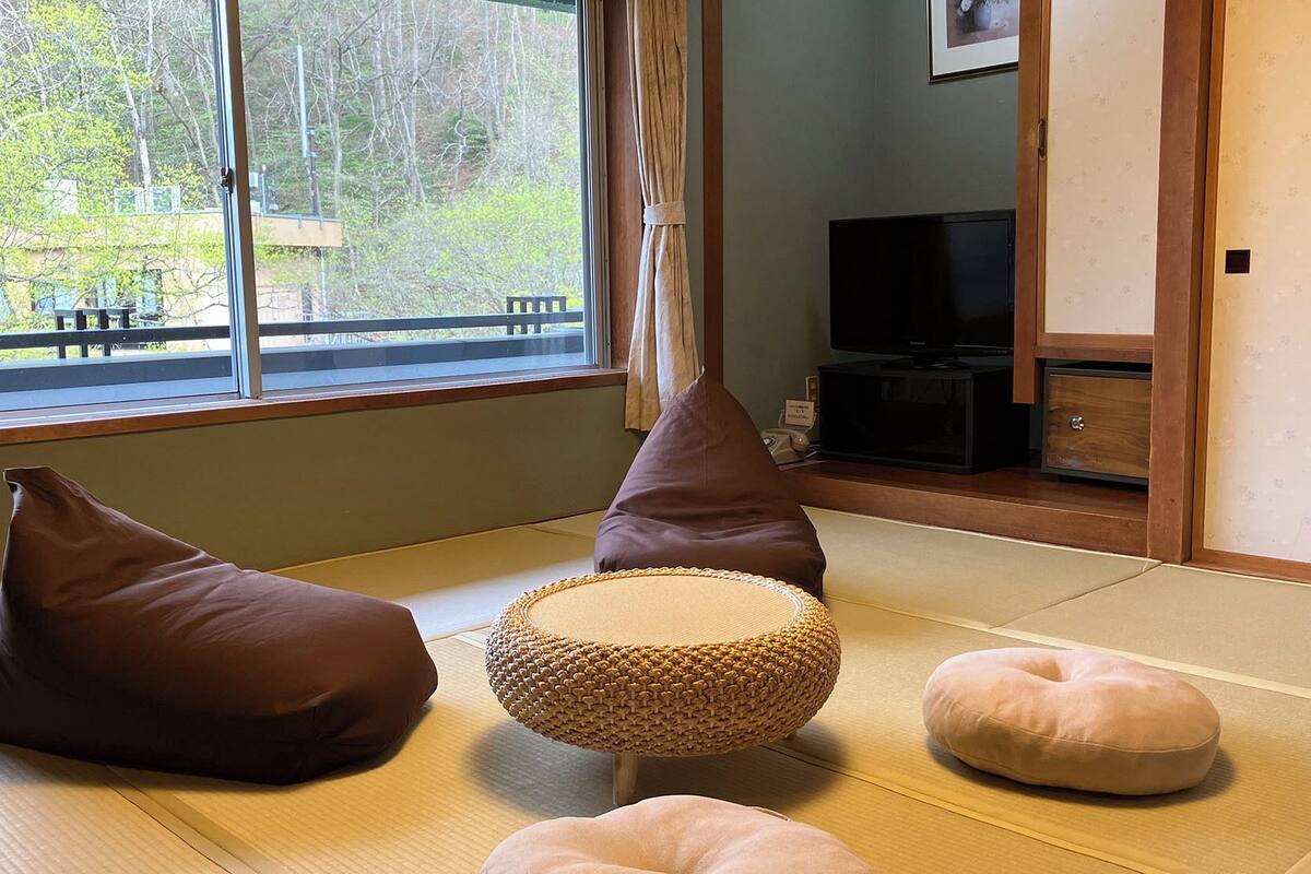 Ein Zimmer mit Tatami-Matten, einem Fernseher und Kissen.