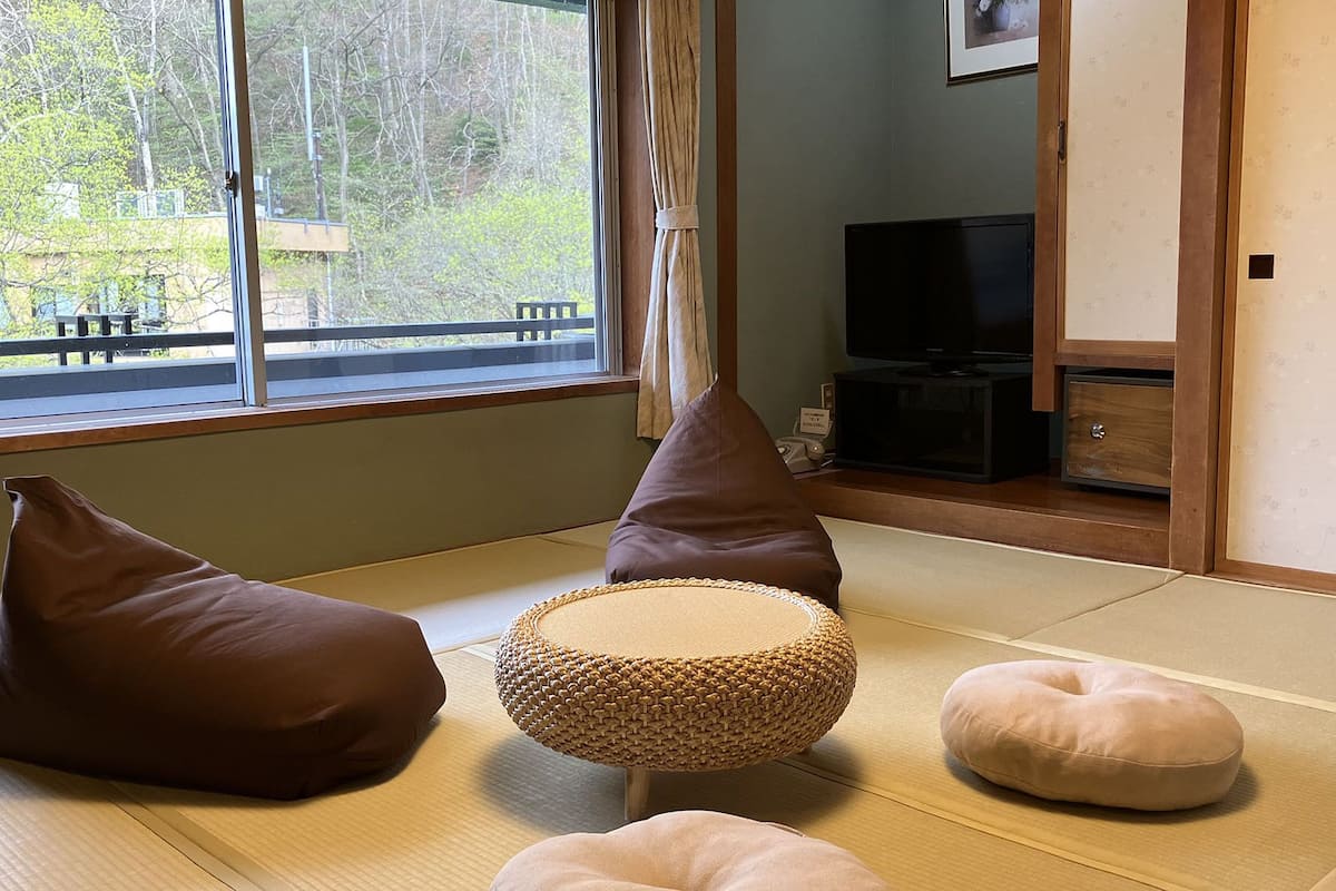 Ein Zimmer mit Tatami-Boden, einem Fernseher und Kissen.
