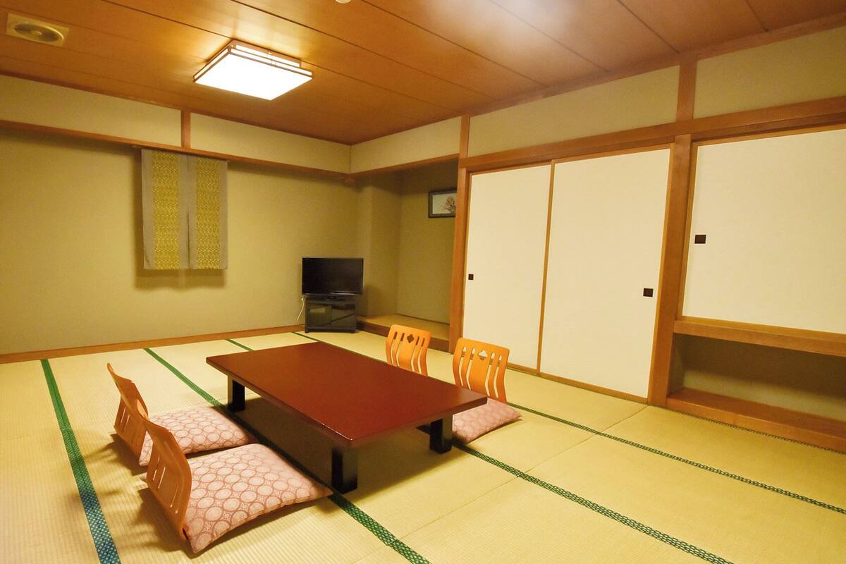 Ein traditioneller japanischer Raum mit Tatami-Böden, einem niedrigen Tisch und einem Fernseher.