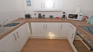 Een keuken met witte kastjes, een houten aanrecht, een magnetron, een waterkoker en een broodrooster.