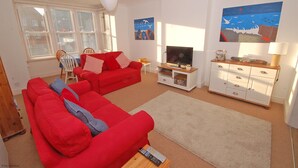 Een woonkamer met een rode bank, een televisie, een witte kast en kunstwerken aan de muren.