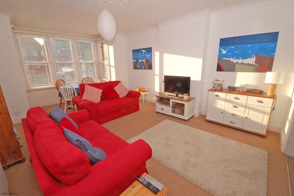 A living room with a red sofa, a television, a white cabinet, and artwork on the walls.