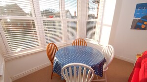 Een kamer met een ronde tafel, bedekt met een blauwe tafelkleed met stippen, omringd door witte stoelen.