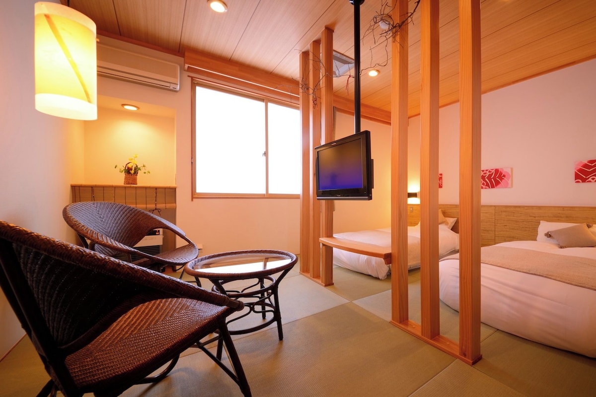A hotel room with a bed, two chairs, a small table, a TV, and a window.