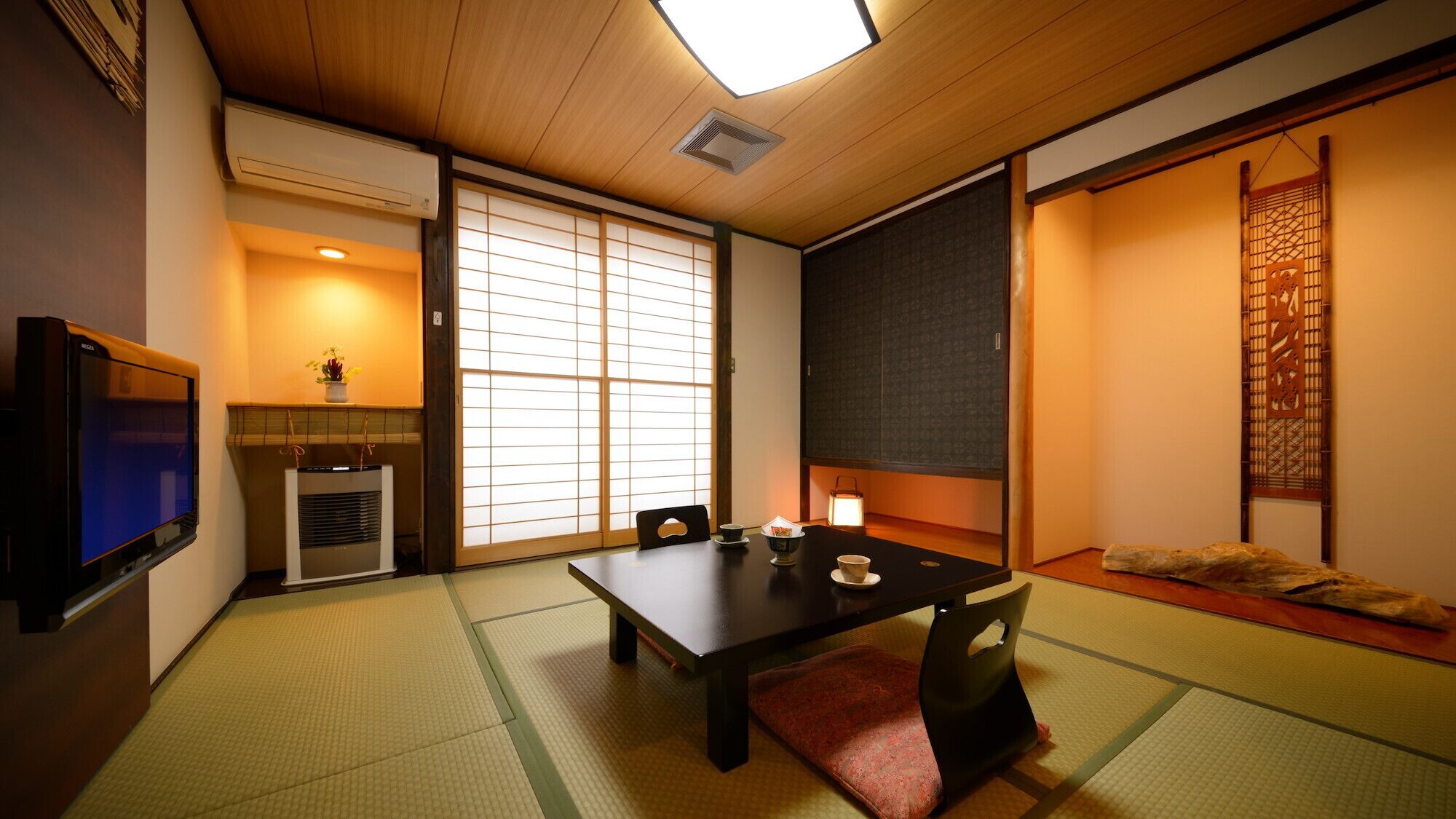 Ein traditioneller japanischer Raum mit Tatami-Böden, einem niedrigen Tisch mit Kissen, Schiebetüren und einem Fernseher.