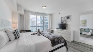 A modern hotel room with a large bed, a desk, a TV, and a view of the cityscape. - Icon Residences (Miami)