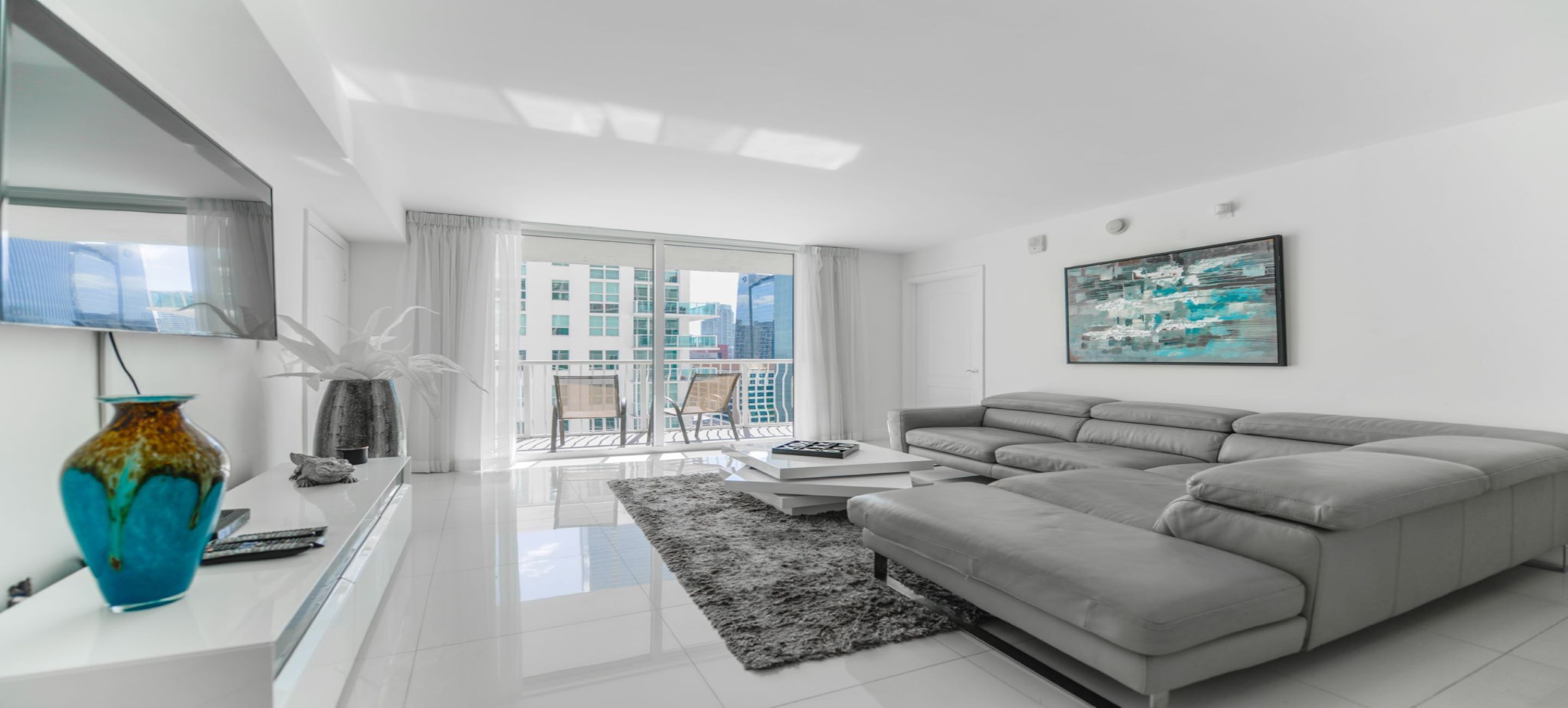 A modern living room with a grey sofa, a coffee table, and a large window with a view of buildings.