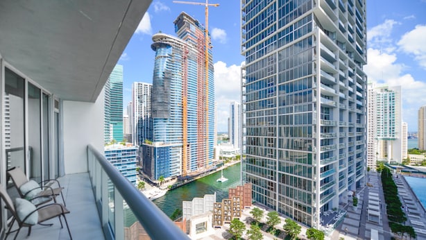 A high-rise building with a glass facade, a construction crane, and a river in the background. - Icon Residences (Miami)
